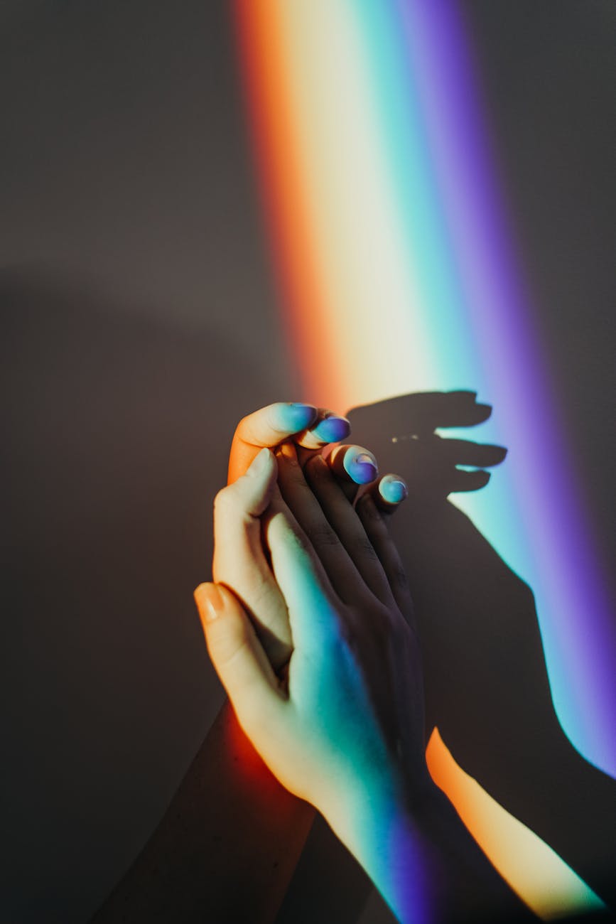 Hands grasping each other with a rainbow colored reflection.